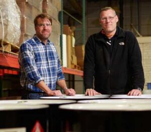 Two Men Standing by Barrels in Warehouse