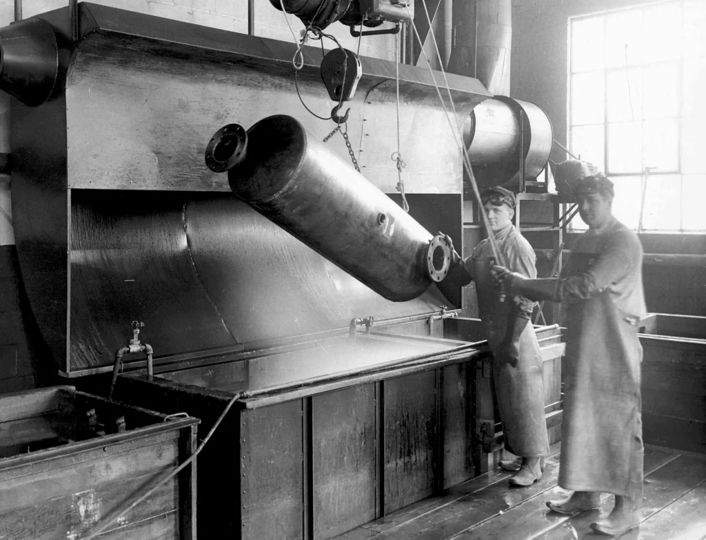 Black and White Photo of workers dipping metal