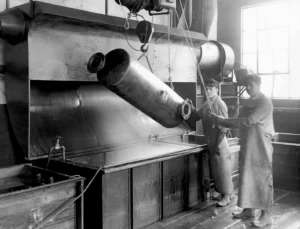 Black and White Photo of workers dipping metal