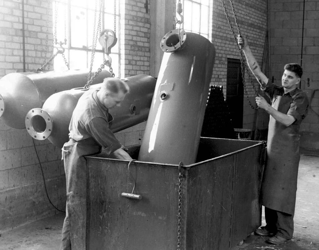 Black and White Photo of workers dipping metal